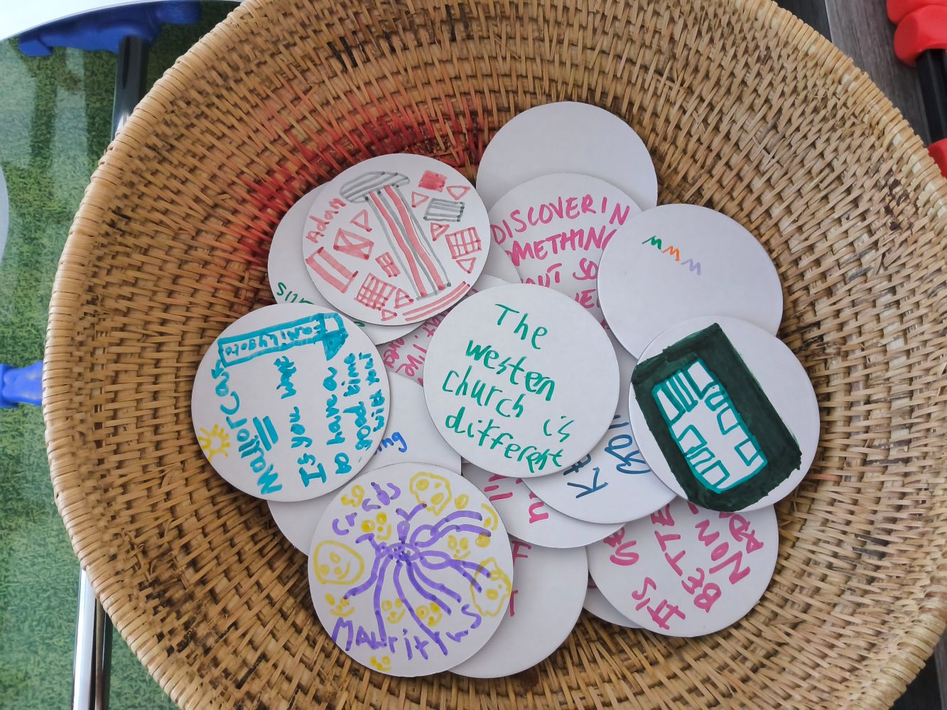 A woven basket full of white card discs on which are written and drawn images and text The Western church is different