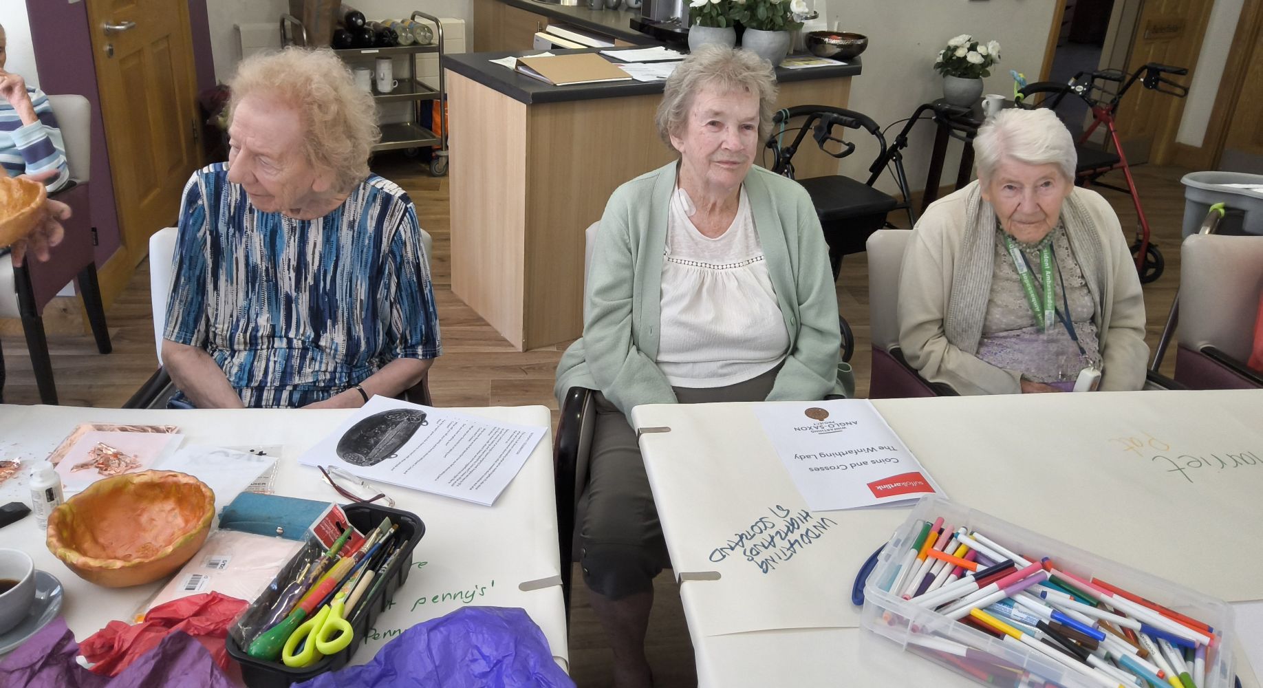 A tow of three ladies seated at a table with an assortment of creative materials in front of them