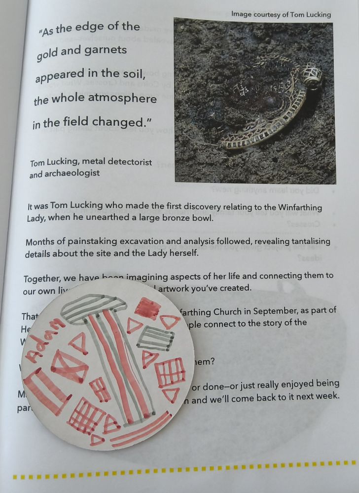An open publication showing image of semi-buried gold pendant with hand drawn disc in bottom left corner with word Adam