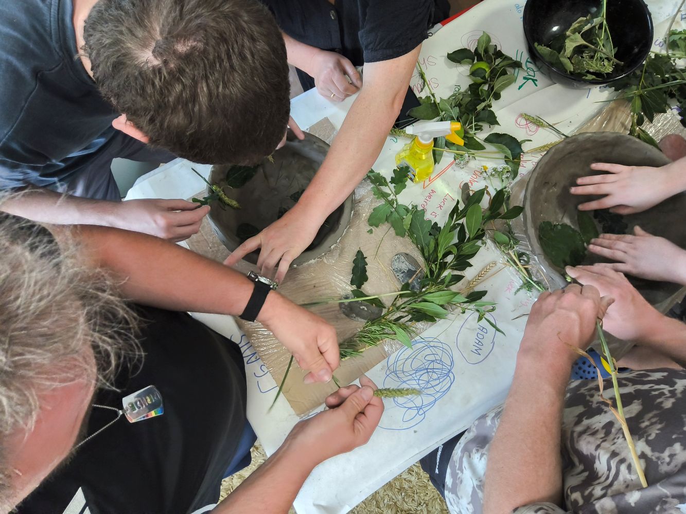 Overhead view of hands pushing leaves and grasses into wet clay bowls