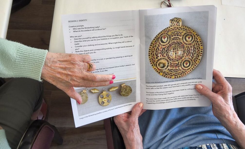 Overhead view of a photograph of a garnet-encrusted gold pendant and a woman comparing the stone in her ring with the image
