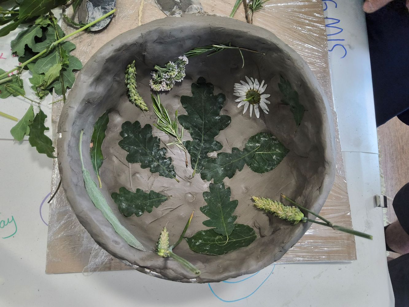 Flowers, seed heads and oak leaves used to line the interior of a clay bowl