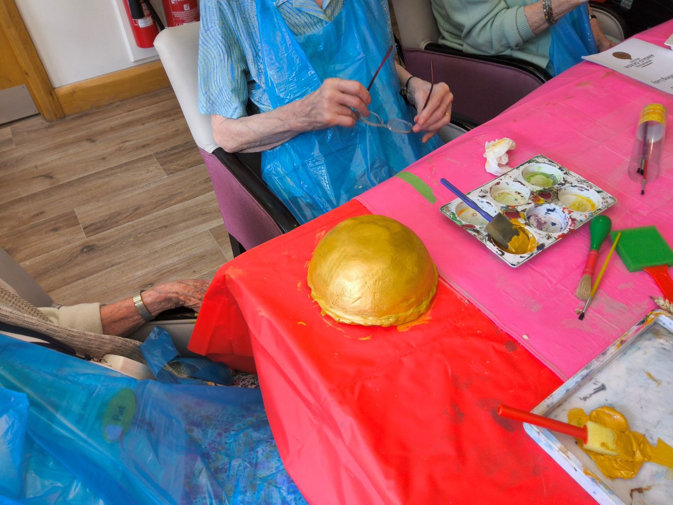 View on an upturned bowl painted gold and assorted arts materials, paints brushes etc on the pink table top