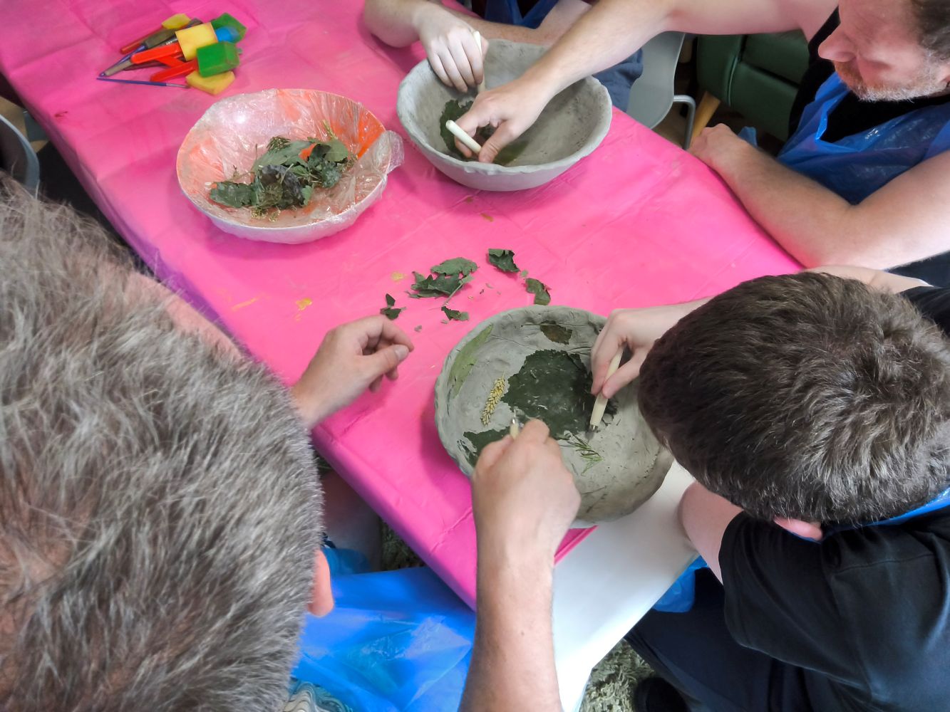 Overhead of group of adults using wooden implements to pick at foliage stuck in clay bowls