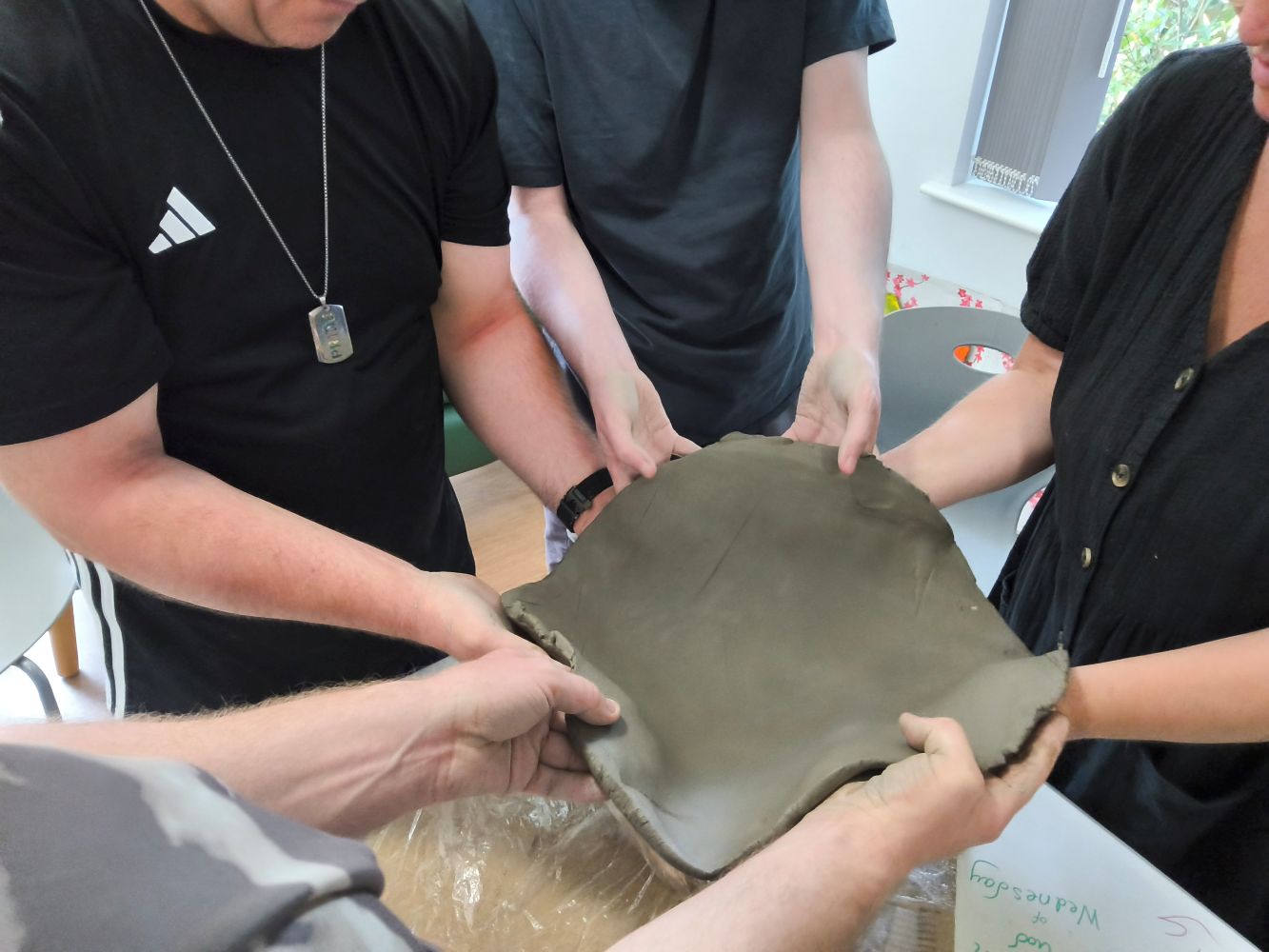 Several people holding a flat piece of clay, ready to place it inside the bowl mould