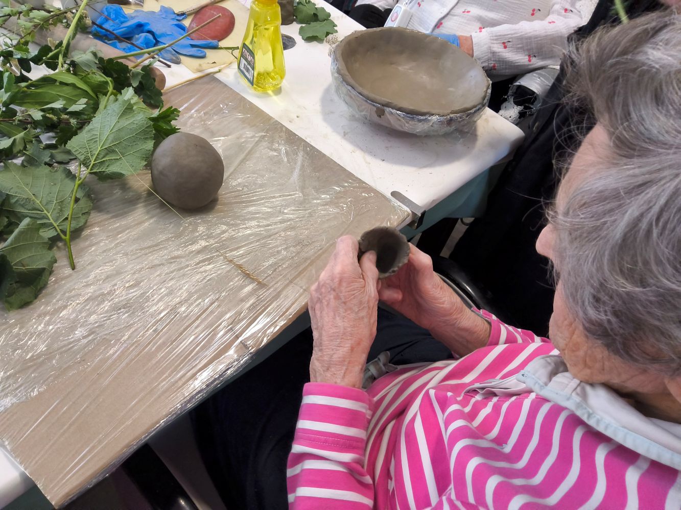 Overhead view of a person in a pink and white striped top working on a small clay pot