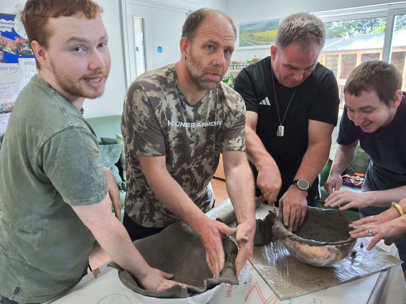 4 adults standing over clay bowls, smoothing the clay into place