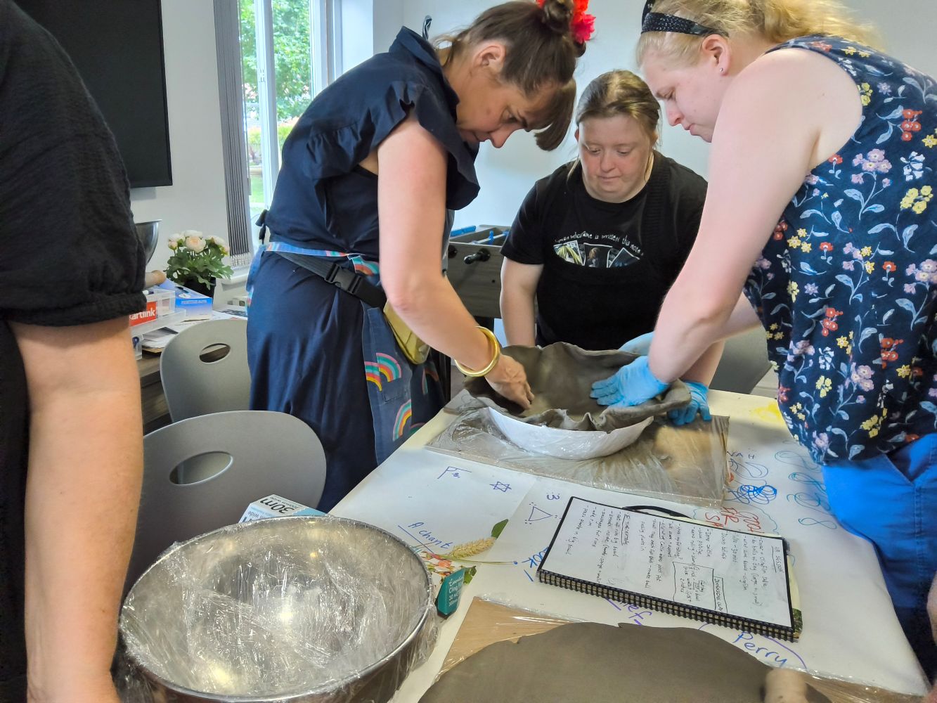 Three people smoothing a large piece of clay into a bowl