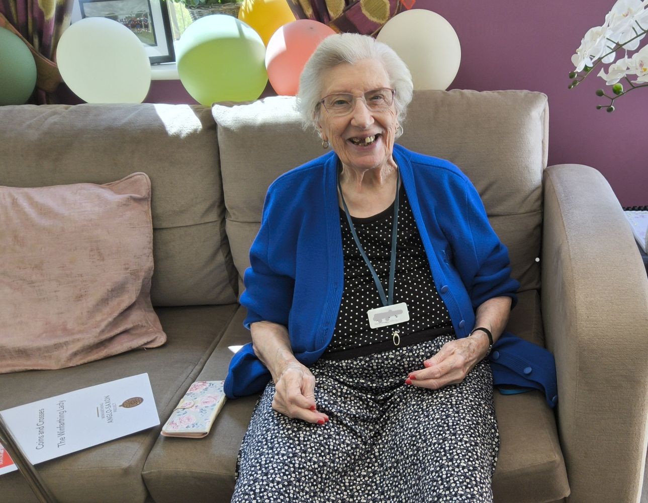 A woman seated on a sofa with a row of balloons behind her