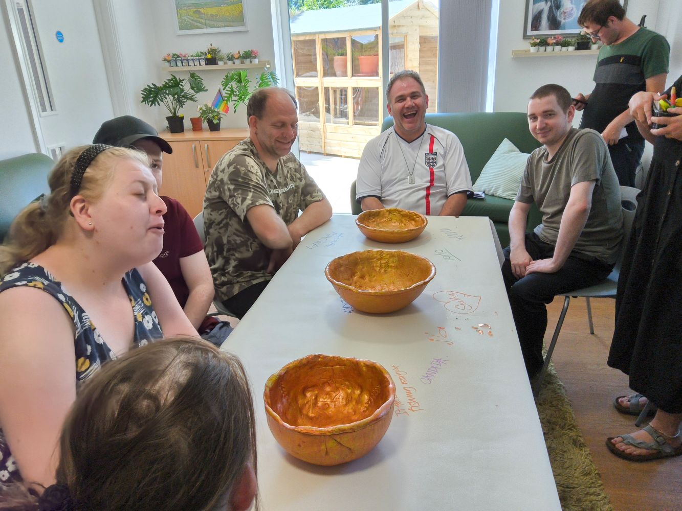 A group of young adults seated around a table on which three gold bowls are lined up down the middle