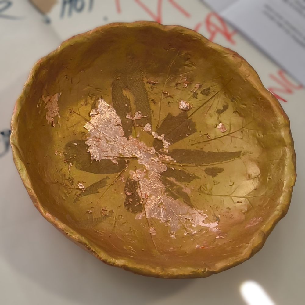 A clay bowl, imprinted with leaf shapes and painted gold and washed with a think bronze paint solution before areas are picked out in gold leaf