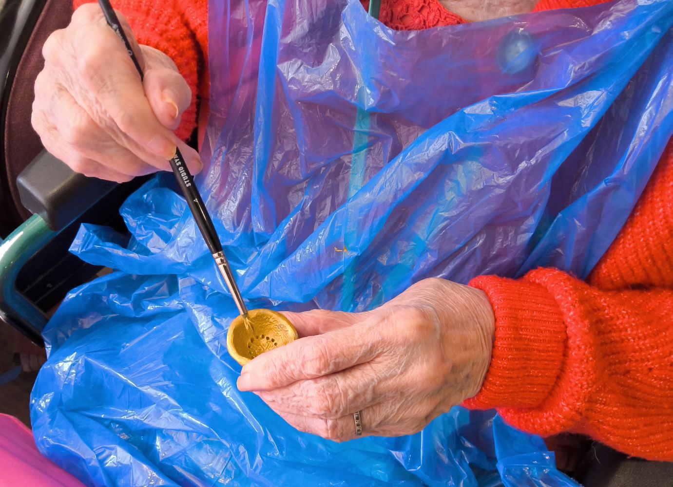 Close up of pair of hands, holding a tiny pin bowl and painting it god