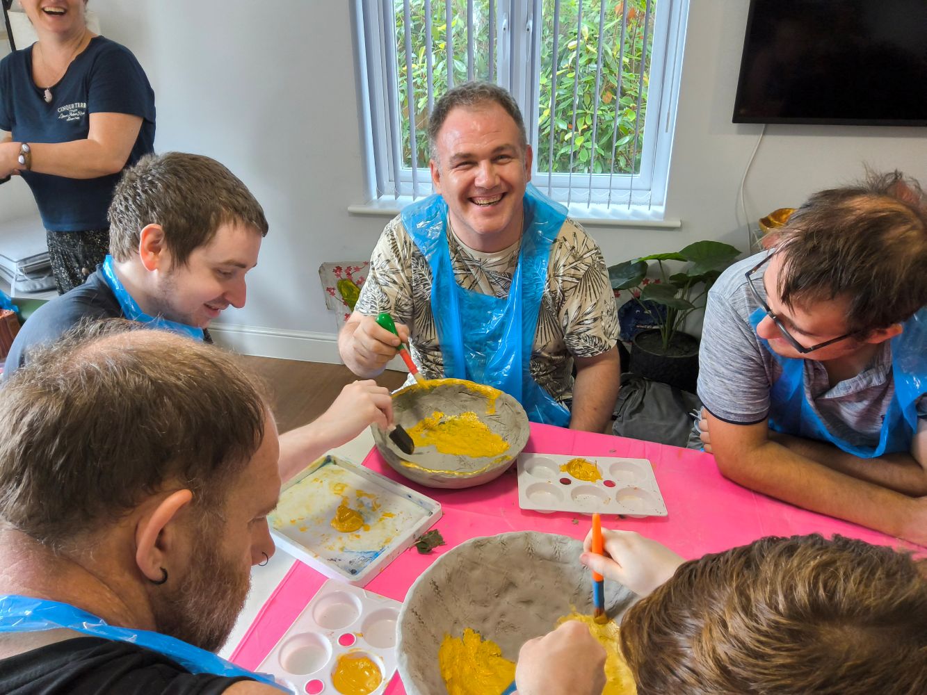 A group of people seated around a table, applying gold paint to clay bowls