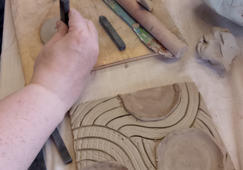 A participant creating a clay tile with circles and lines
