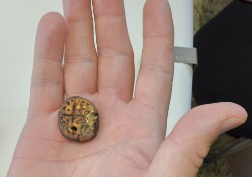 An imprinted and marked metal clay disc in the palm of a hand