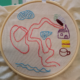 Embroidery with a building and a cup and a river and clouds and a pink path.