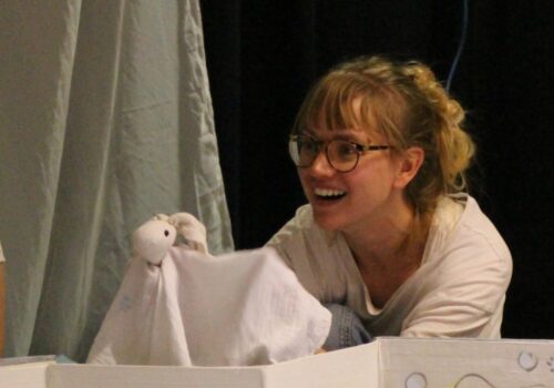 Performer with a puppet popping up behind a screen.
