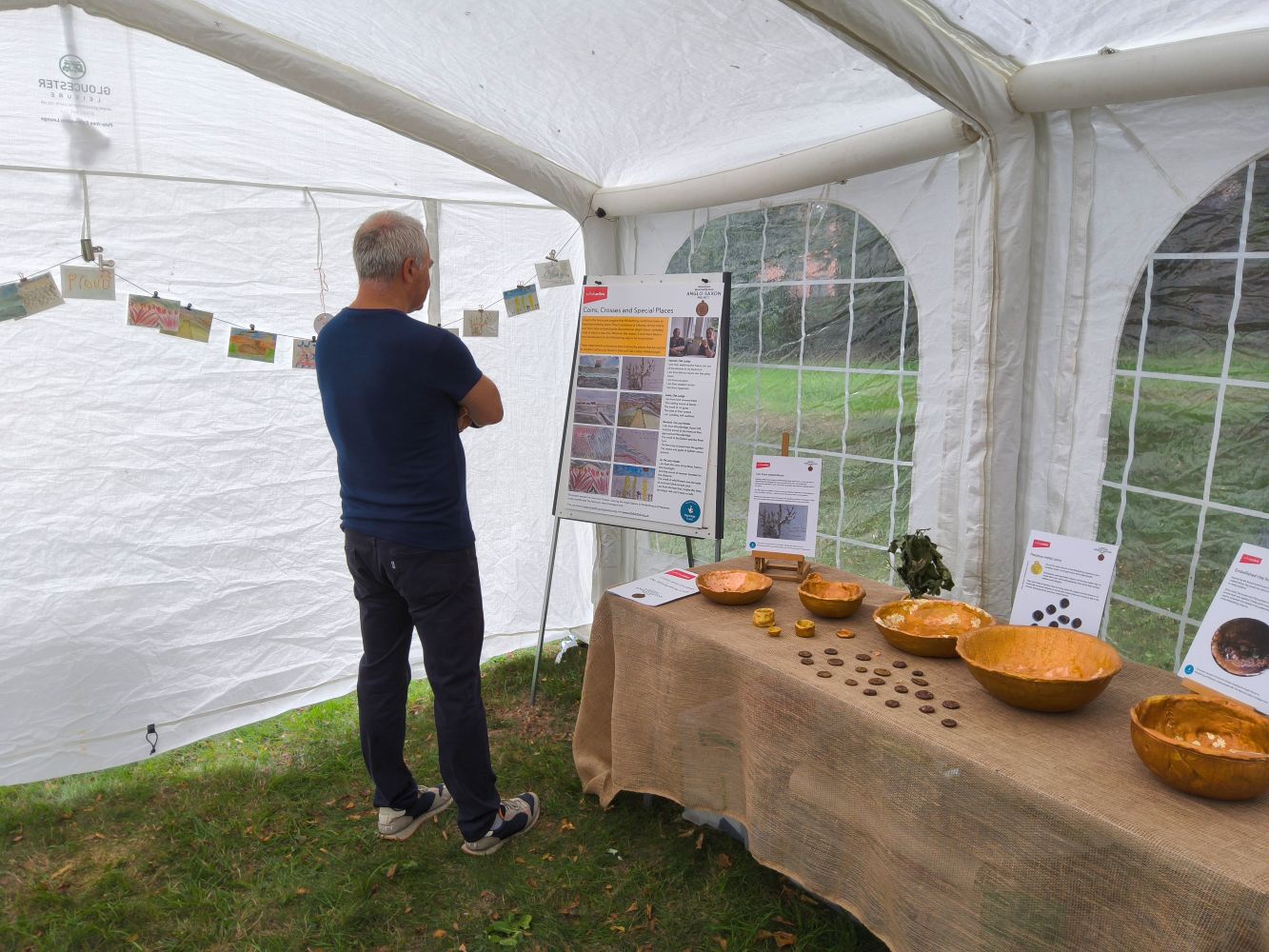 A member of the public reading an information board. To his right is a hessian-covered table with gold bowls and coins displayed on it