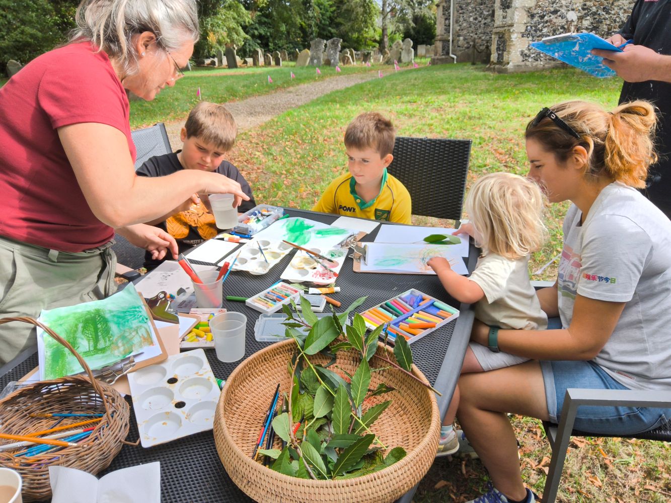 A group of children and adults gathered around a table covered with art materials