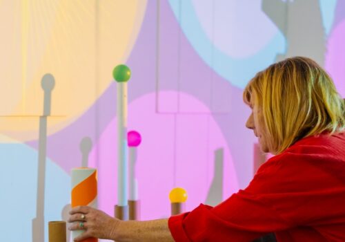 Artist holding a striped tube next to others in front of a wall with coloured circles projected onto it.